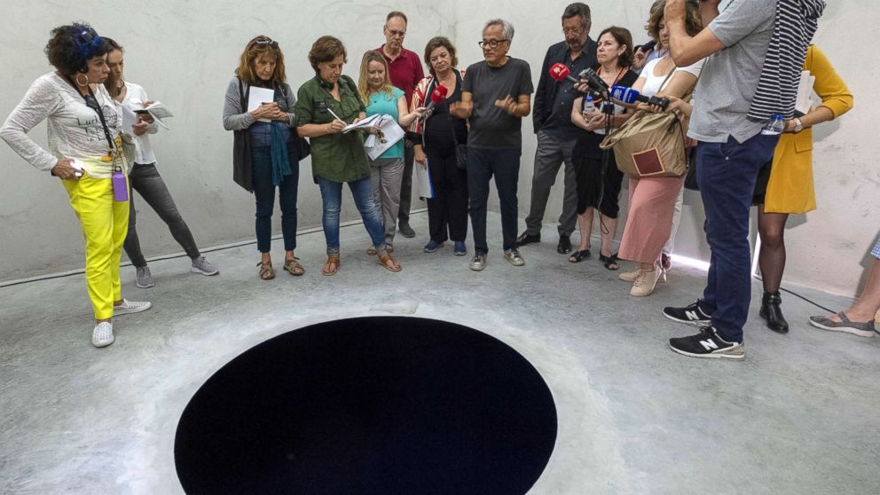 People at art exhibit taking notes and thinking about around a hole in the floor that is very real
