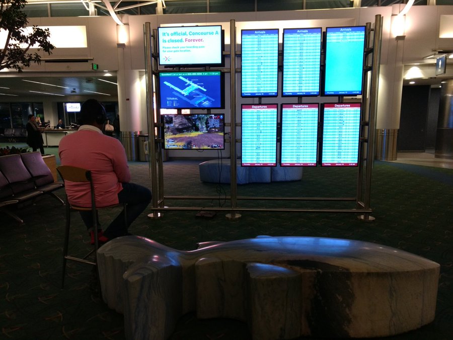 A Gamer (Man) Takes over Portland Airport Monitor to Play Battle Royale Game Apex Legends