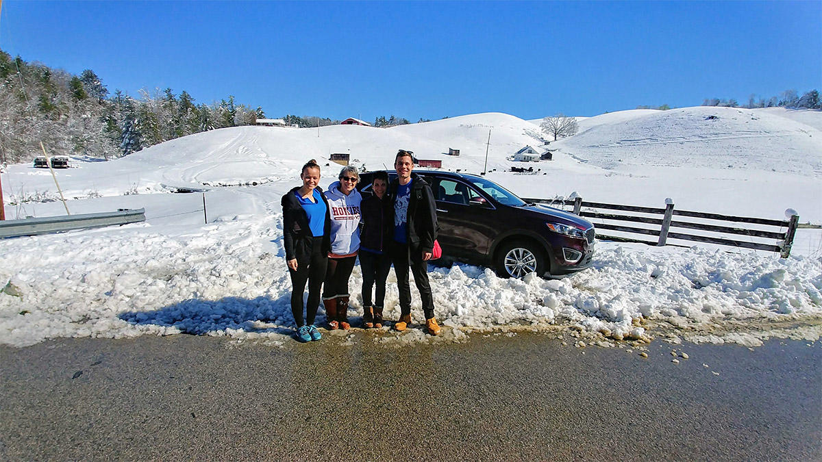 Three people stand on a snowy roadside by a car