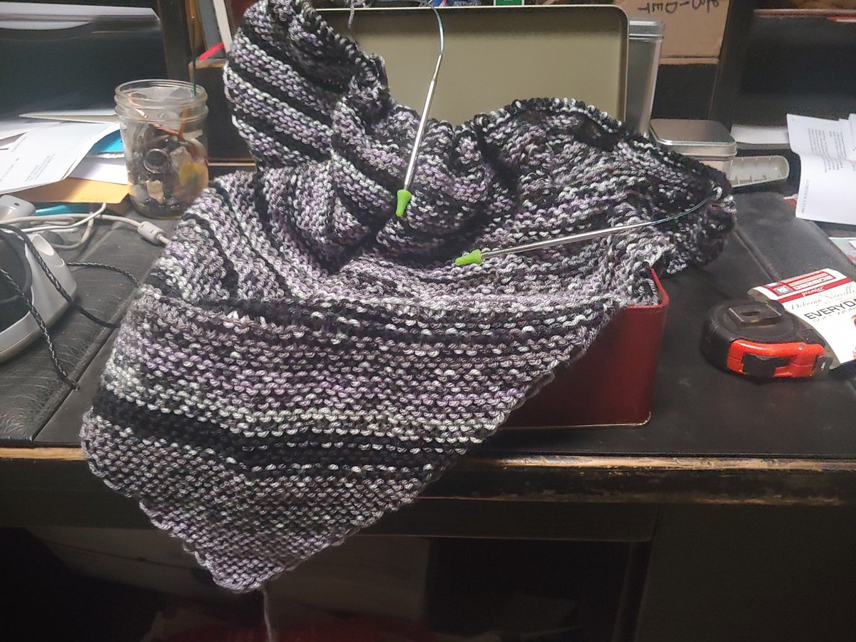A sizable triangle of knitted black grey and purple variegated yarn draped over a tin.