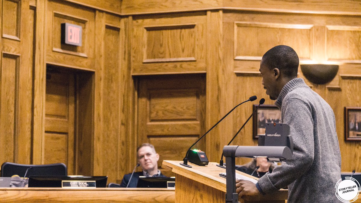 A young black man stands at a podium and testifies at a Sioux Falls City Council meeting. The Storyteller Journal logo appears in the bottom right.