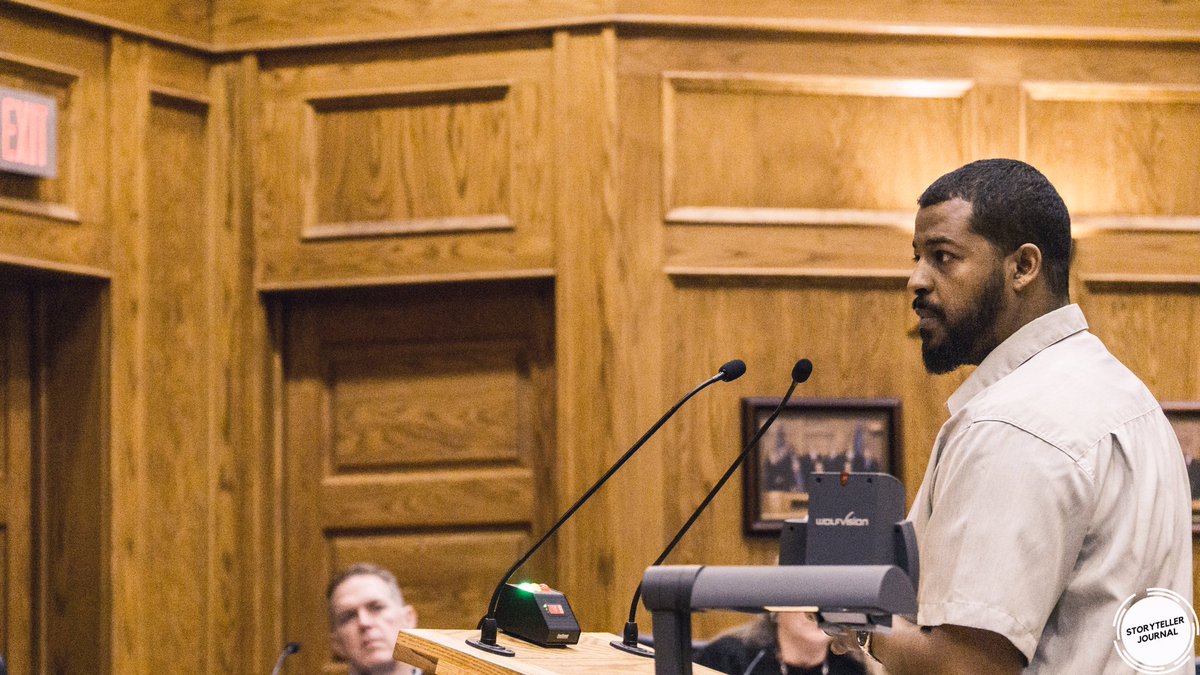 A black man with a beard stands at a podium and testifies at a Sioux Falls City Council meeting. The Storyteller Journal logo appears in the bottom right.