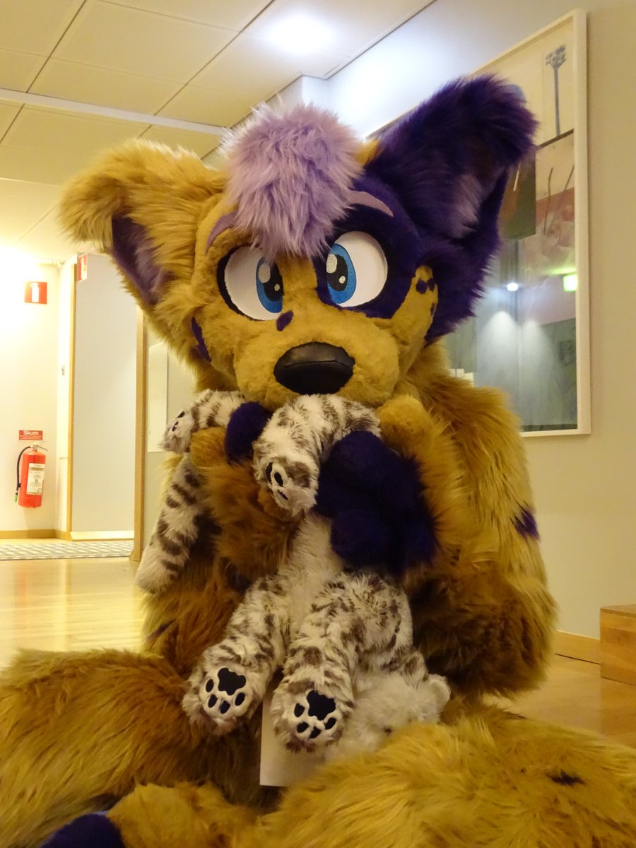 Photo of the Irie fursuit holding a snow leopard plushie upside down