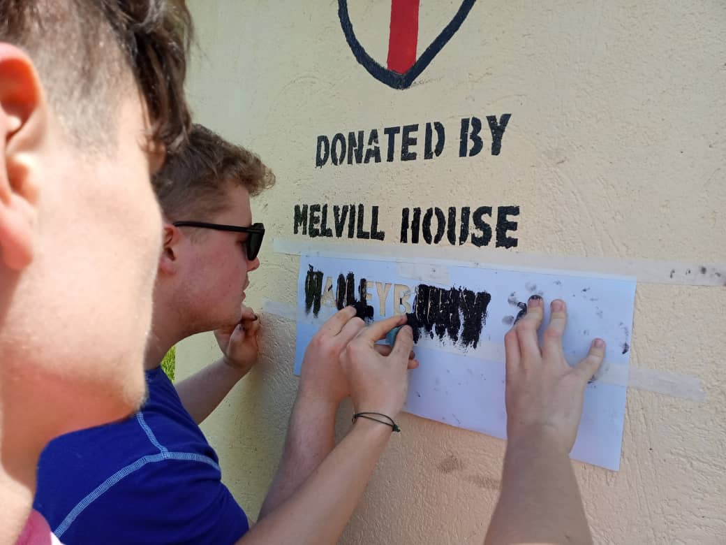 HYTUganda's tweet photo. HYT's new volunteers Ed Holroyd and Rob Douglas diving straight in with some painting at RAVO (Refuge for Aids Victim Orphans). This rainwater harvesting tank, donated by @MelvillHouseUK provides safe water to 371 students! @HaileyburyUK https://t.co/bjgQqAgA1t