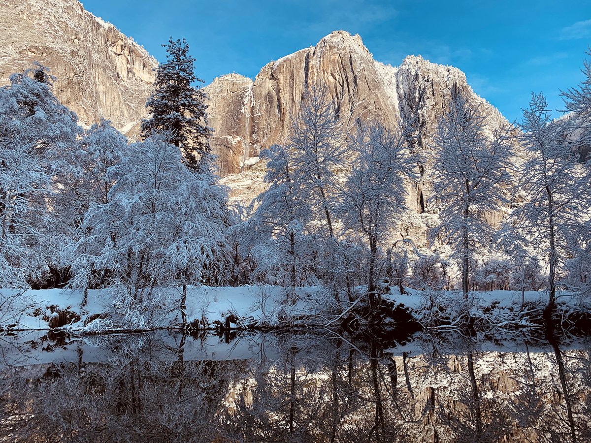 Morning light makes the valley walls glow. Snow-covered trees line the riverbank.