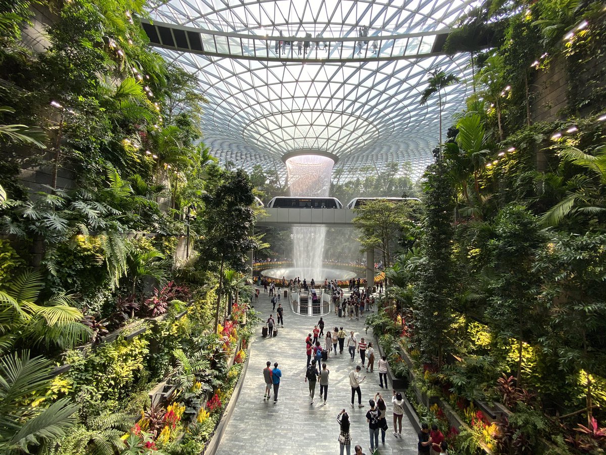 A massive indoor waterfall with a glass ceiling and foliage all around.