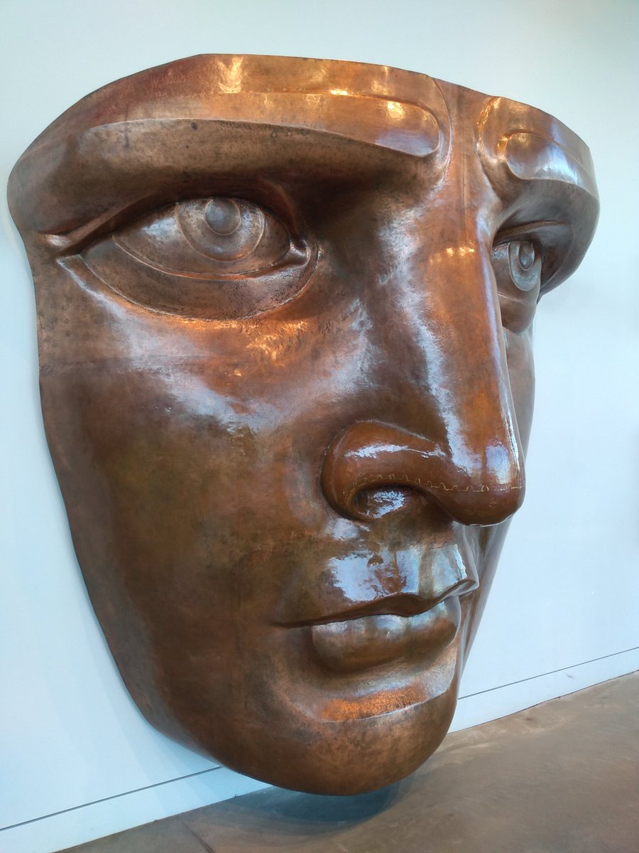 Close up photo of the replica face hanging on a white wall at the Statue of Liberty Museum.