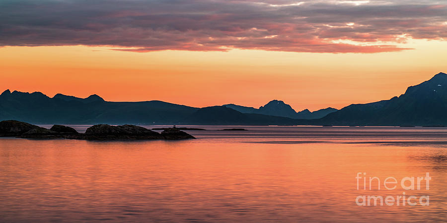 Long exposure photograph of a sunset over the sea. The nearby mountain peaks and islets create a dark barrier that contrasts with the orange sky and water.
