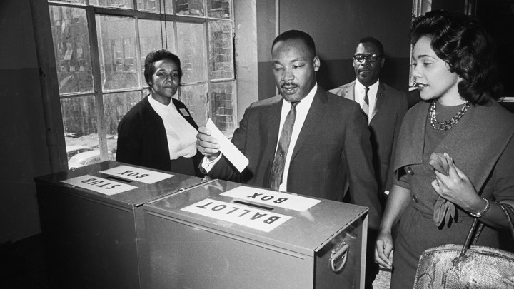A black and white photo of Dr. King casting his ballot in Atlanta in 1964 as Coretta looks on.