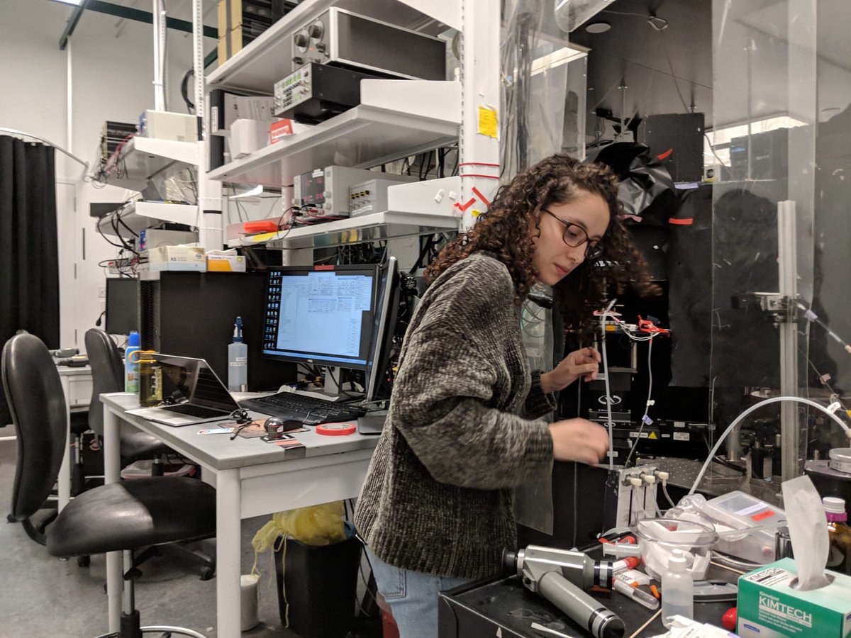Nancy standing in a lab full of computers and scientific instruments. She is working on one of the instruments.