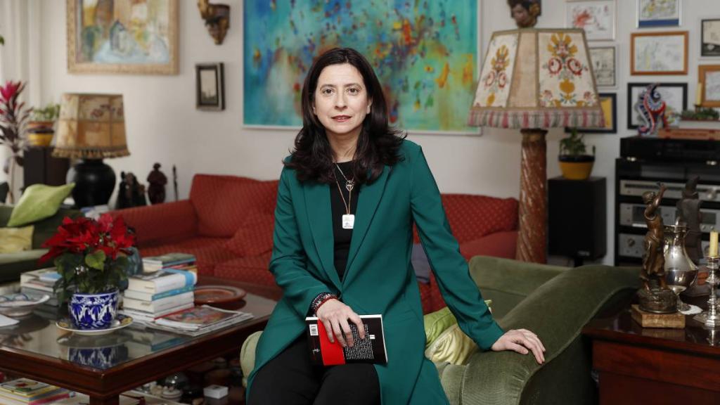 Professor Ana Merino sitting at the front of her desk while holding a book.
