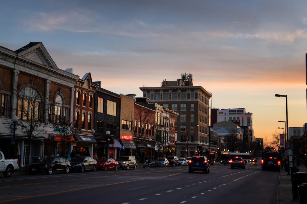 Cars drive along Clinton Street in Iowa City during dusk.