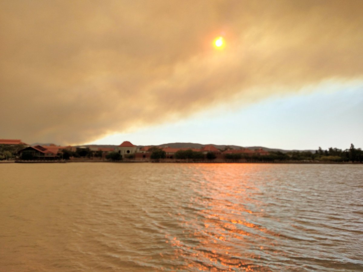 A cloud of brown smoke rises from the Orroral Valley in the background while red sunlight glints across Lake Tuggeranong.