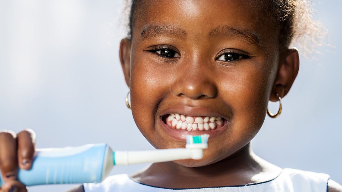 A young girl smiles while brushing her teeth.