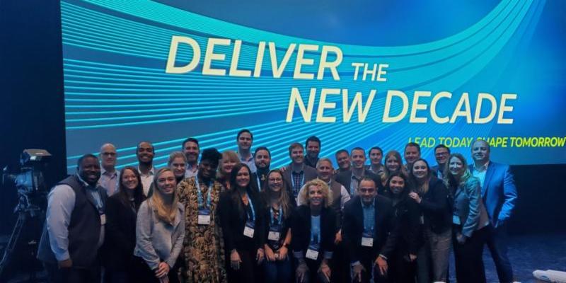 Employees standing in front of presentation titled "Deliver the New Decade"