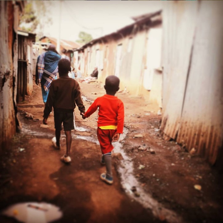 foto di due bambini che camminano tendosi la mano camminando per la baraccopoli di Soweto in Kenya