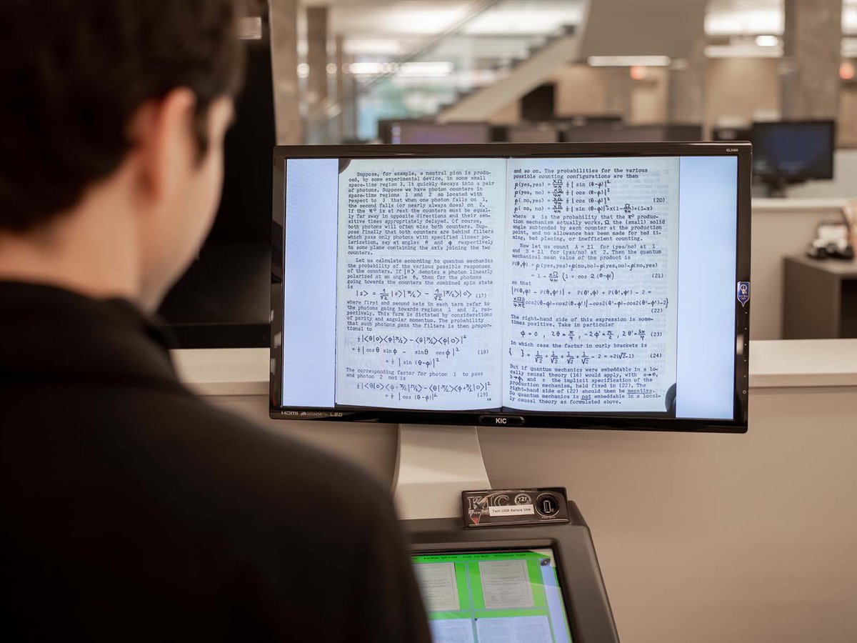 A computer screen is seen over the shoulder of the a man. The screen has a page from Epistemological Letters newsletter about quantum mechanics on it.