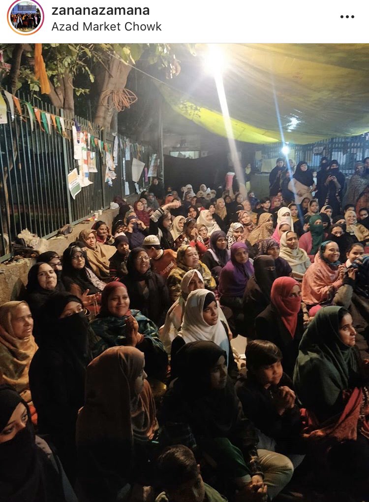 A large group of women sitting on the streets in the night, in protest, watching a performance.