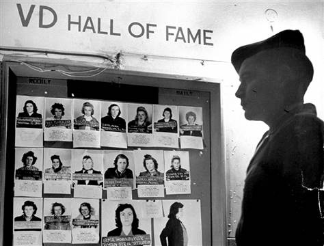 Американский солдат стоит у стенда с фотографиями немецких женщин, разносчиц венерических заболеваний. Германия 1945