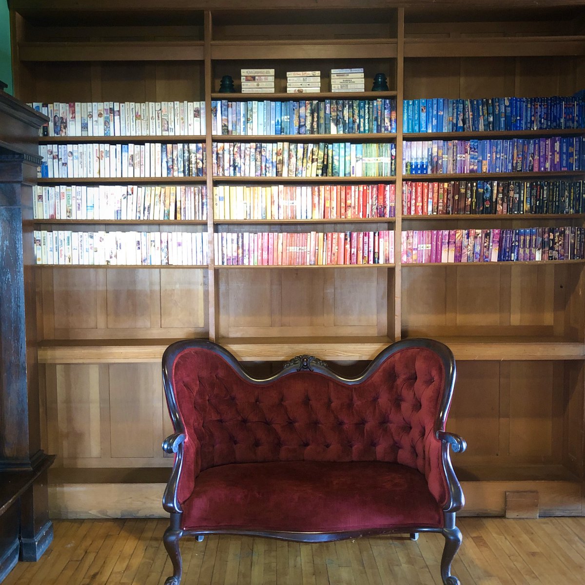 Red settee in front of a bookcase full of paperbacks arranged in color order