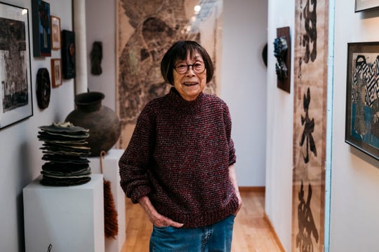 Marie Woo stands smiling in a gallery featuring her ceramic sculptures.