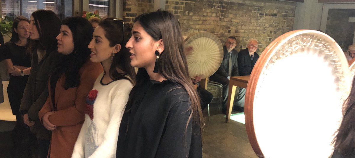 Four Yezidi women singing while others play tambourine-style instruments.