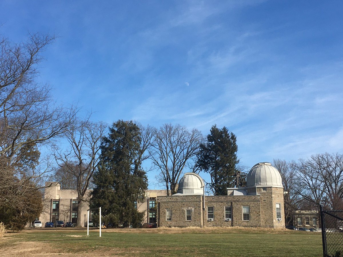 Stone building with two white domes underneath blue skies with a quarter moon visible in the sky.