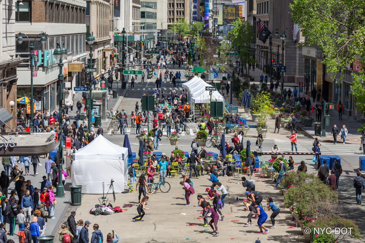 An aerial shot of car free earth day. Foreground shows people participating in a dance class. Background shows various tents and people walking on a car free street. 