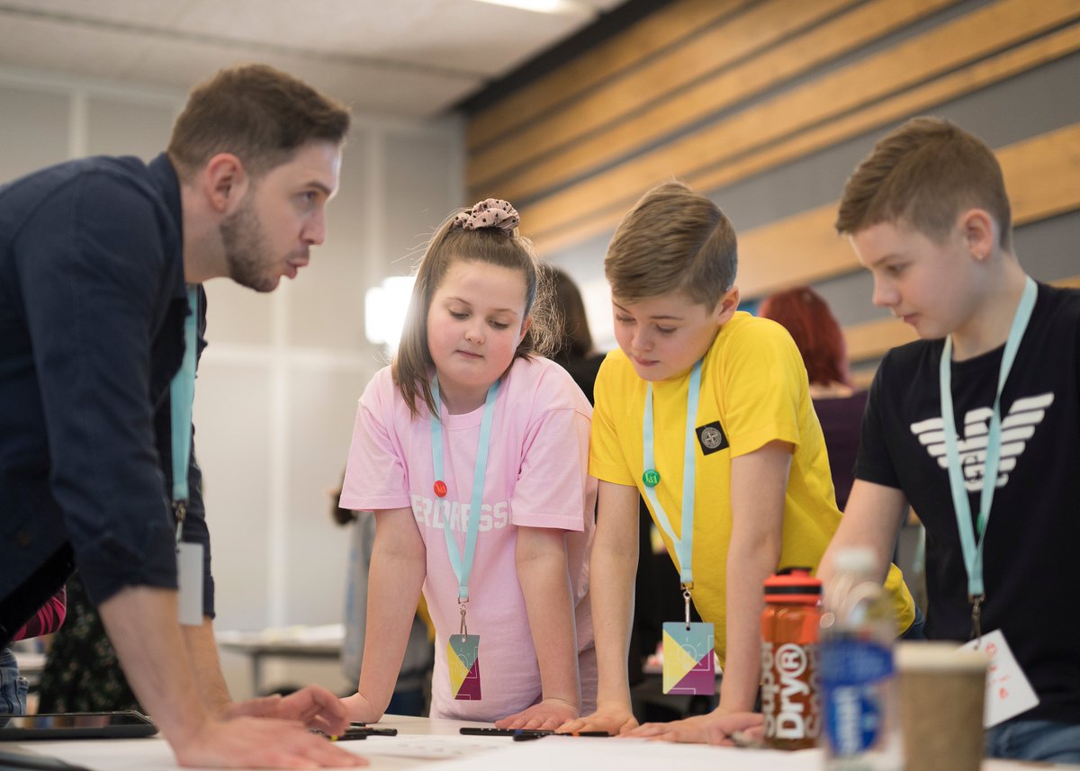 Image of a designer in dialogue with three children during a design jam. 