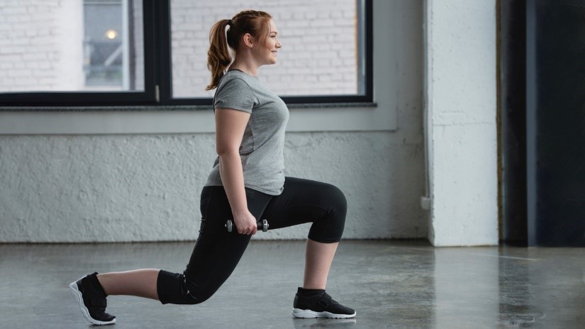 Image: A woman does lunge exercises with hand weights, taking care not to bend her knee beyond 90 degrees.