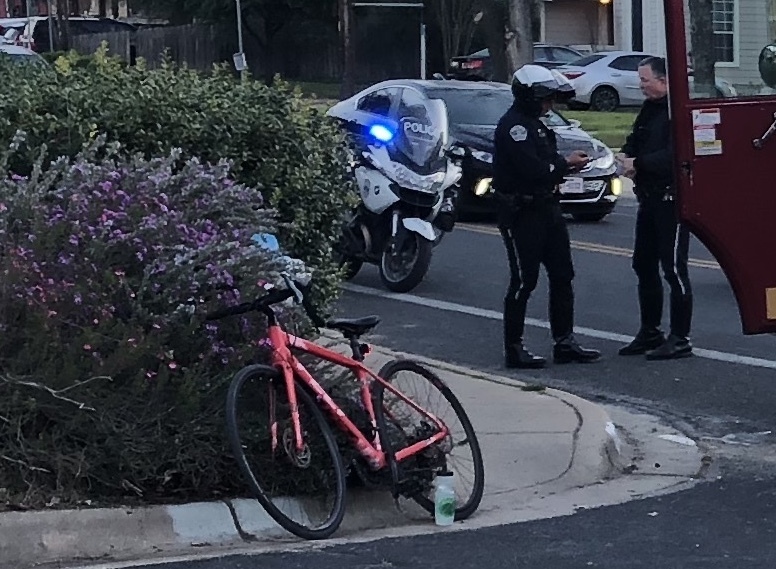 Photo of bike propped against vegetation and 2 APD officers talking.