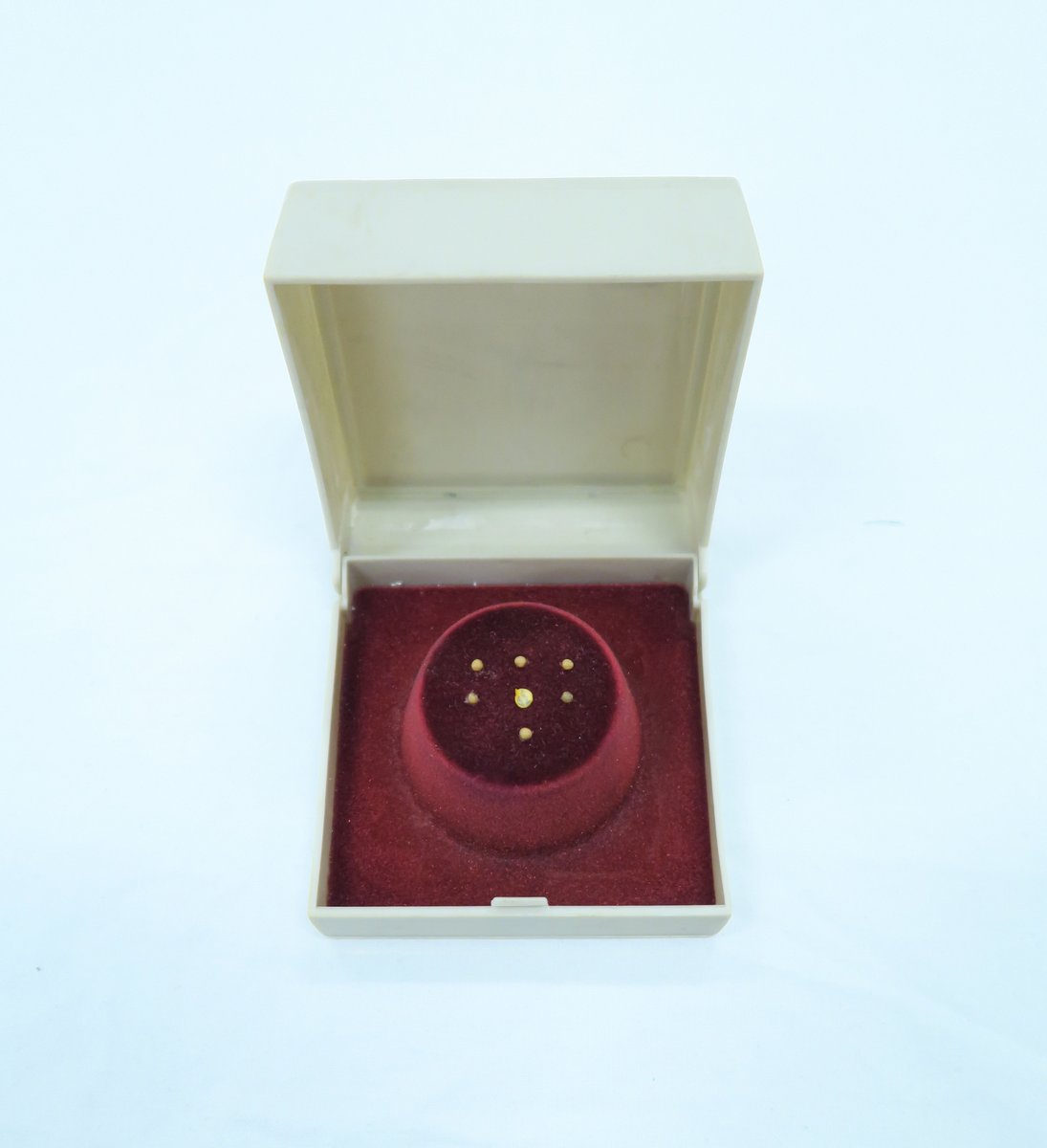 Seven mustard seeds are mounted on a red velvet stand within the 3" x 3" white box. Each seed is individually illustrated with micro writing. On three seeds in middle level are images of individuals, and on other four seeds in above and below level are texts that is too tiny to dechiper.  