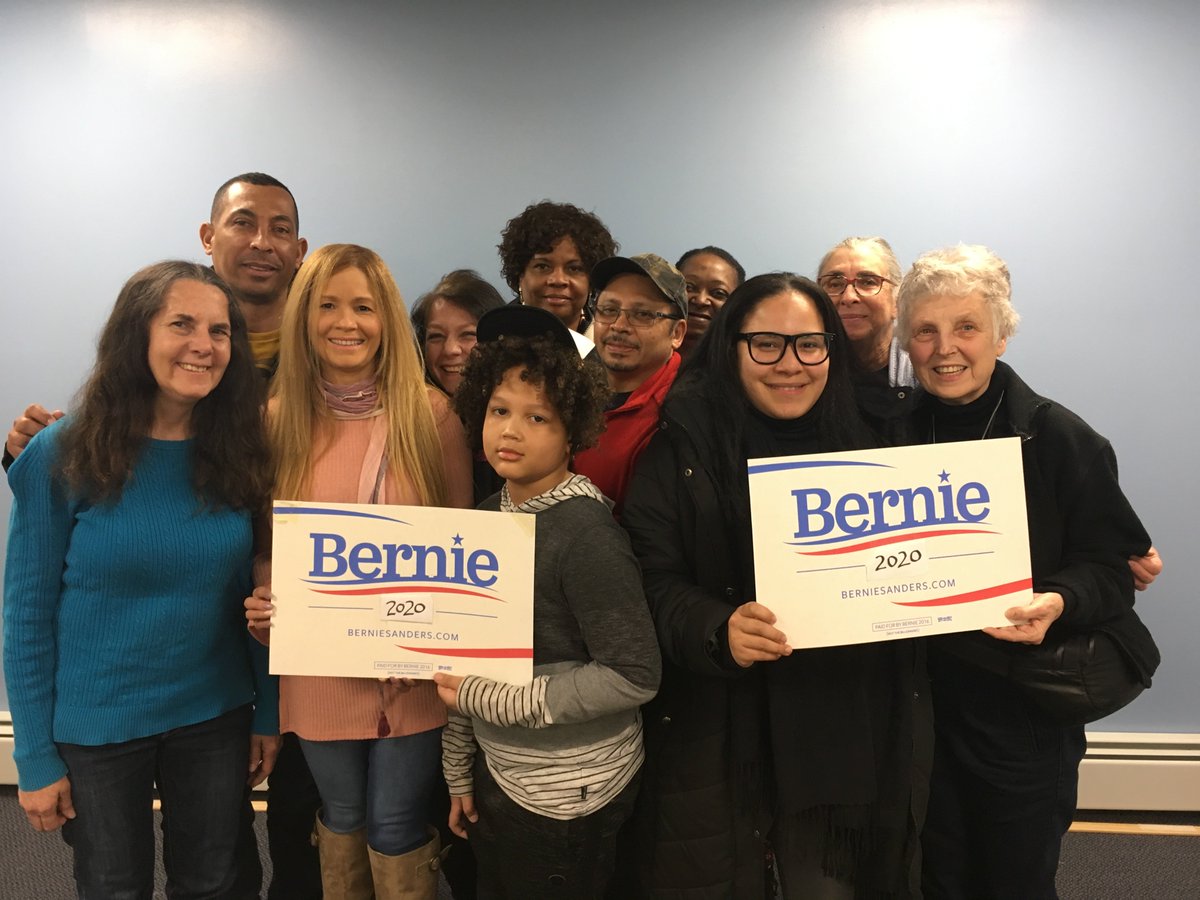 Photo of 11 people of diverse backgrounds posed holding 2 Bernie Sanders campaign signs.