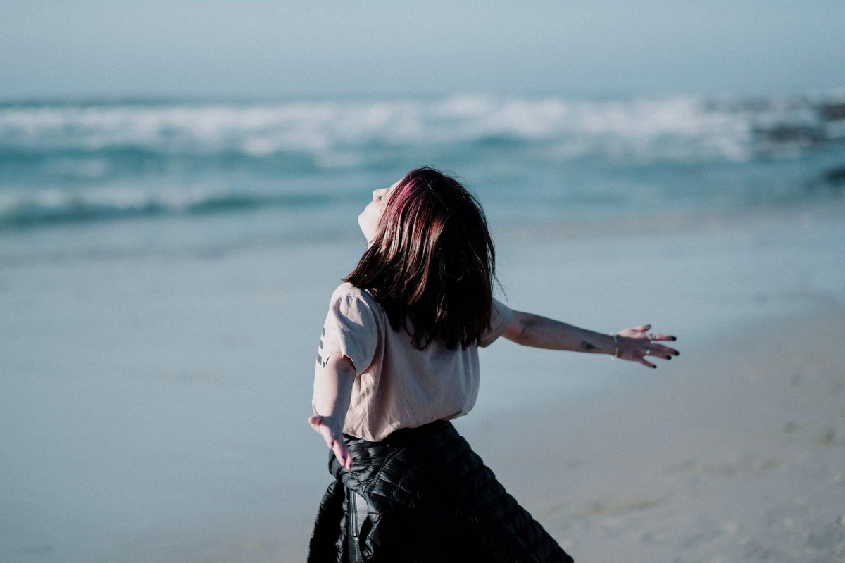 A Netlify team member throws back her arms, raises her face to the sky and soaks in the crisp atmosphere at the beach in Monterey