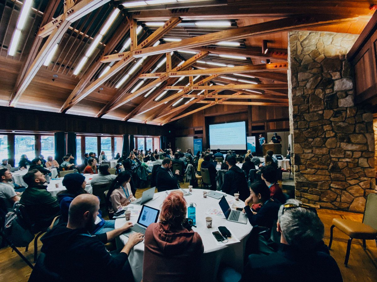 The founders of Netlify talk on stage to a room full of the team seated at round tables in a stone and timber lodge.