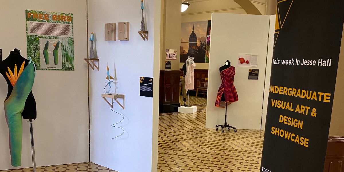 A sign stands that reads "Undergraduate Visual Art & Design Showcase." Nearby you can see displays of clothing and artwork.