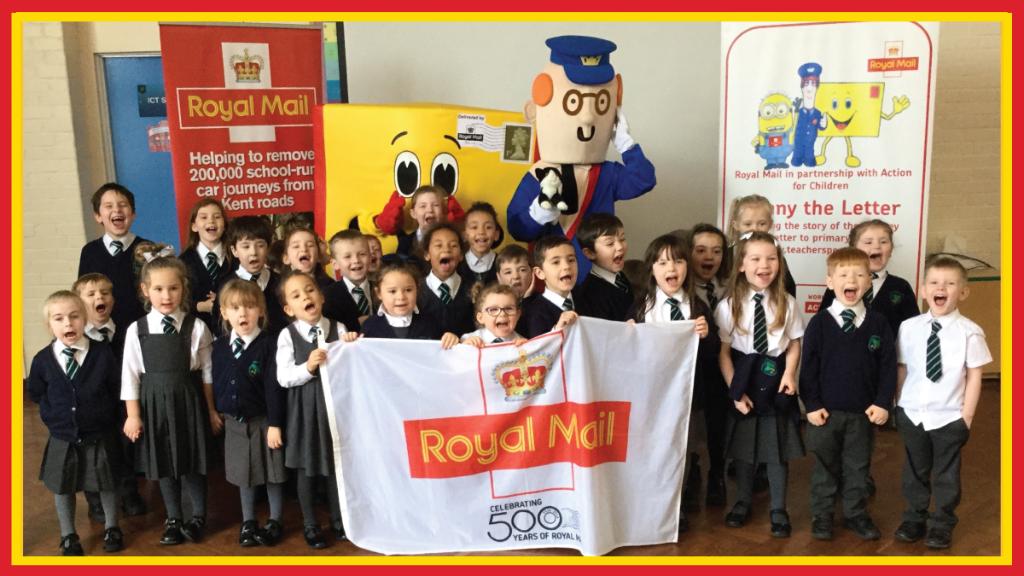 School children stand next to Postman Pat and Lenny the Letter while holding a Royal Mail banner.