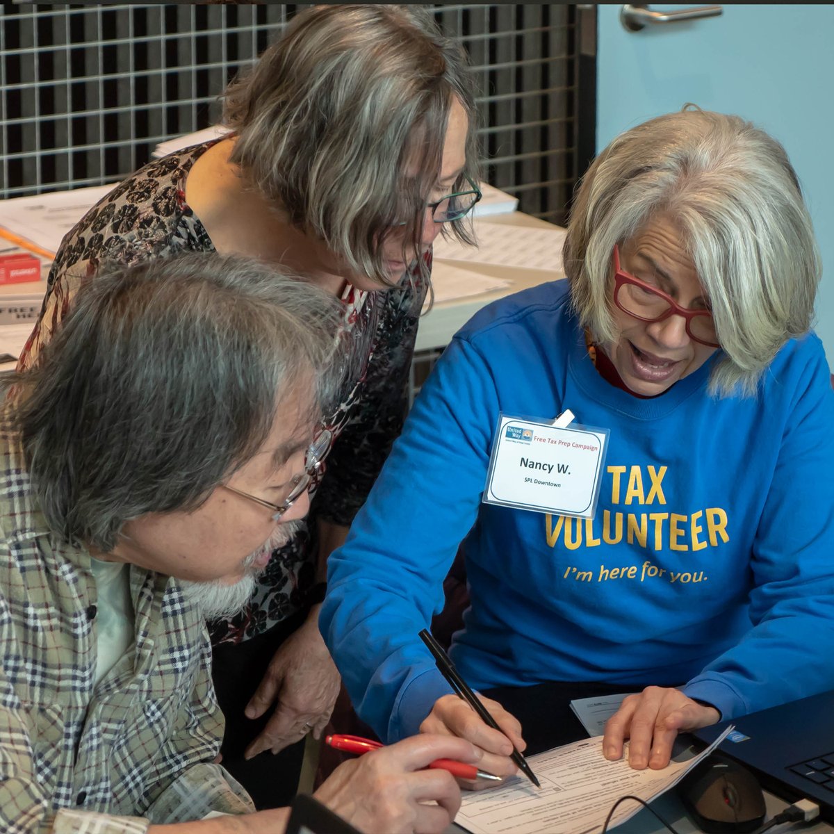 Tax help volunteer assisting two people.