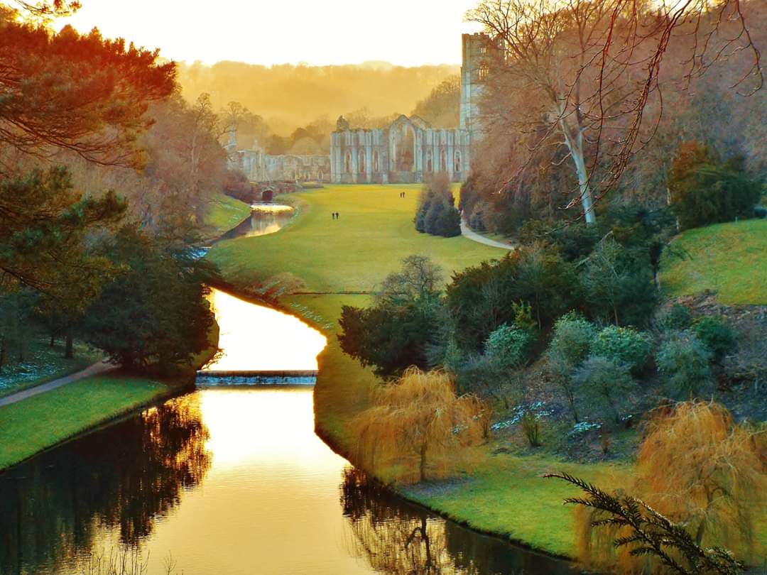 Ruins of Fountains Abbey in the background with a river winding its way towards them.