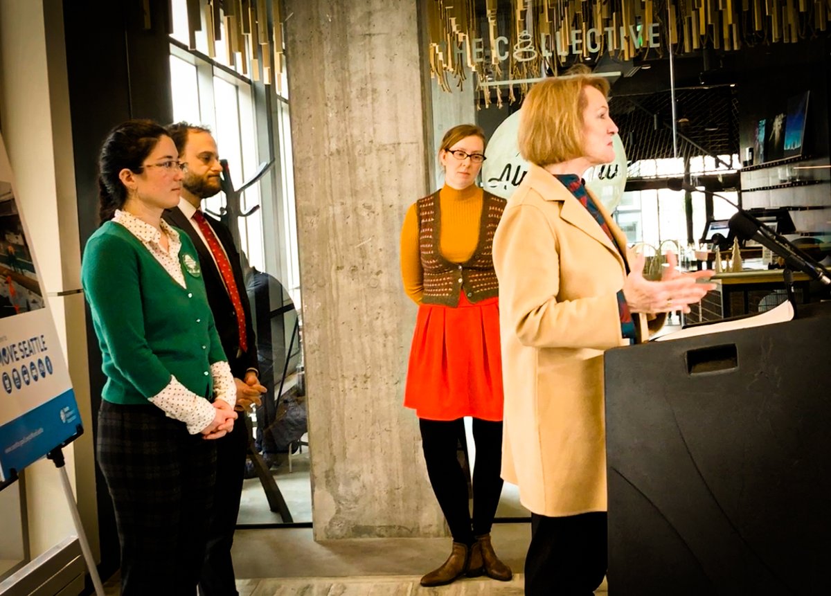Photo of Mayor Jenny Durkan speaking at a podium. Three people stand behind her.