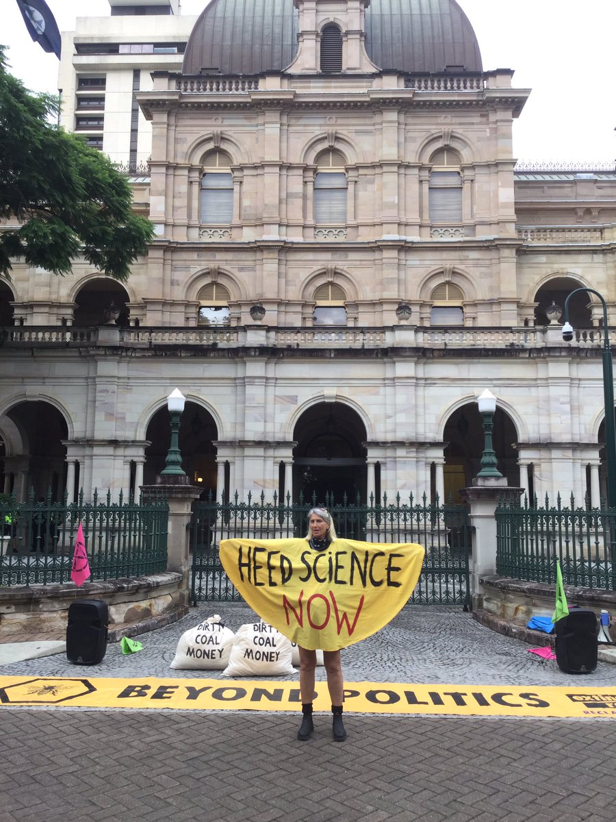 An activist in front of Parliament House, wearing "Heed Science Now". Piles of bags saying "dirty coal money".