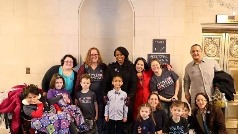 photo of a group of families (adults and children) with Congresswoman Pressley, all smiling at the camera