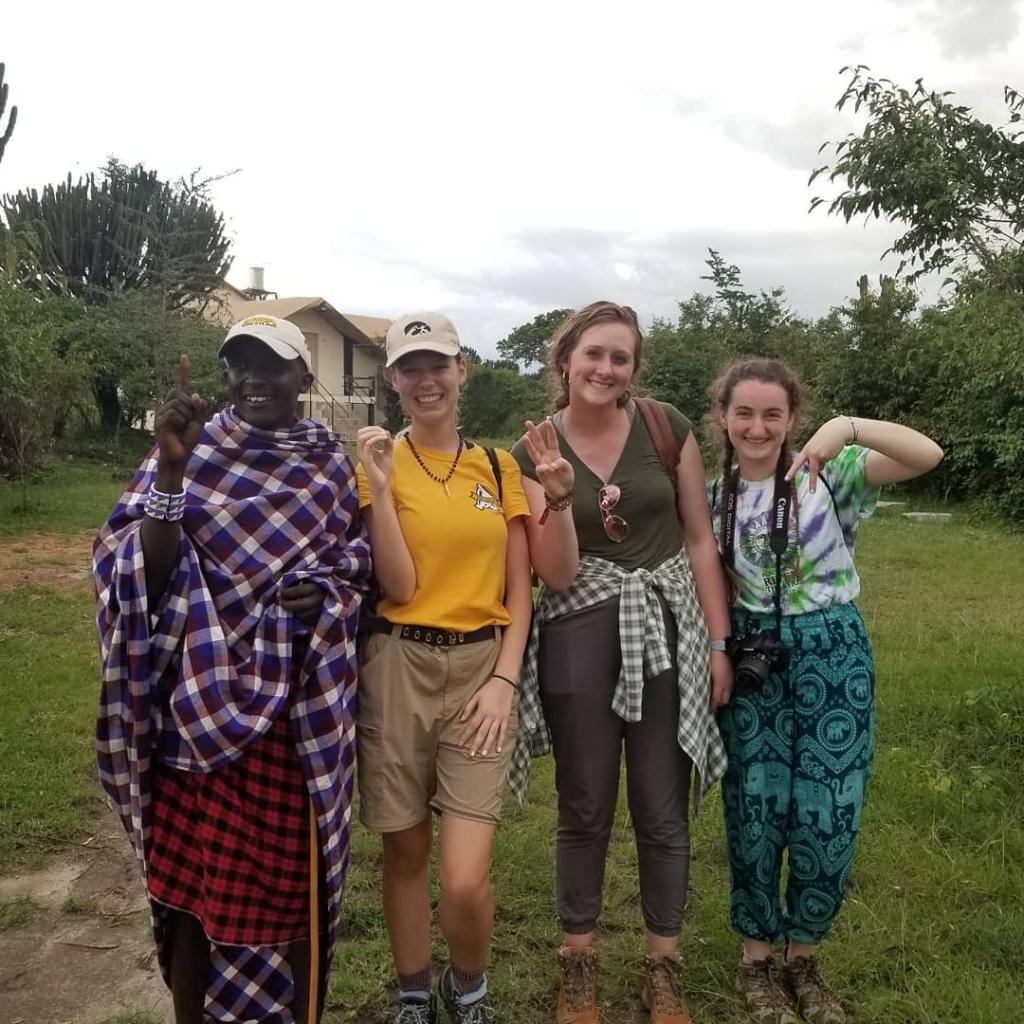Four people stand in a line and spell out I-O-W-A with their fingers.