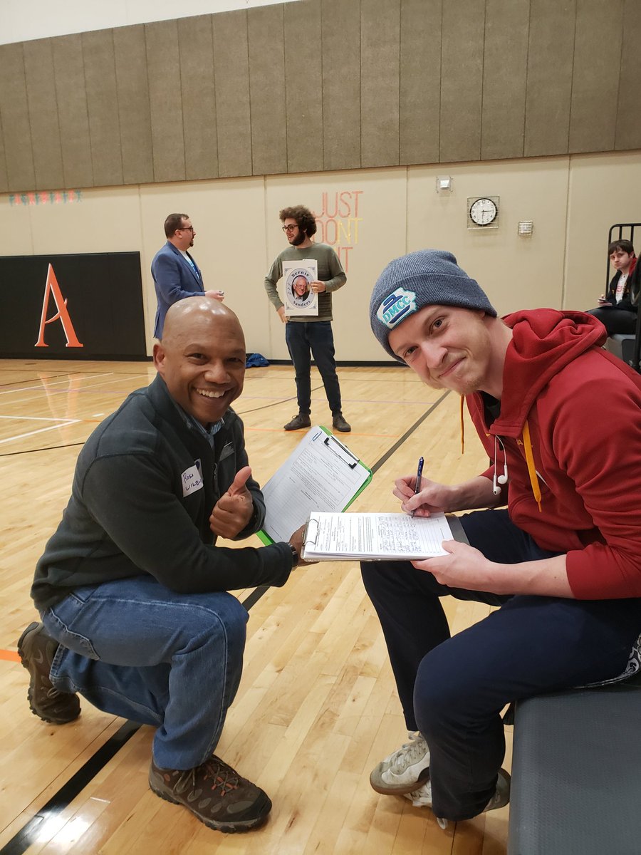 Representative Wilburn kneeling on the gymnasium floor while a Caucus attendee signs his nomination petition for re-election to the Iowa House of Representatives in the June 2nd, 2020 primary