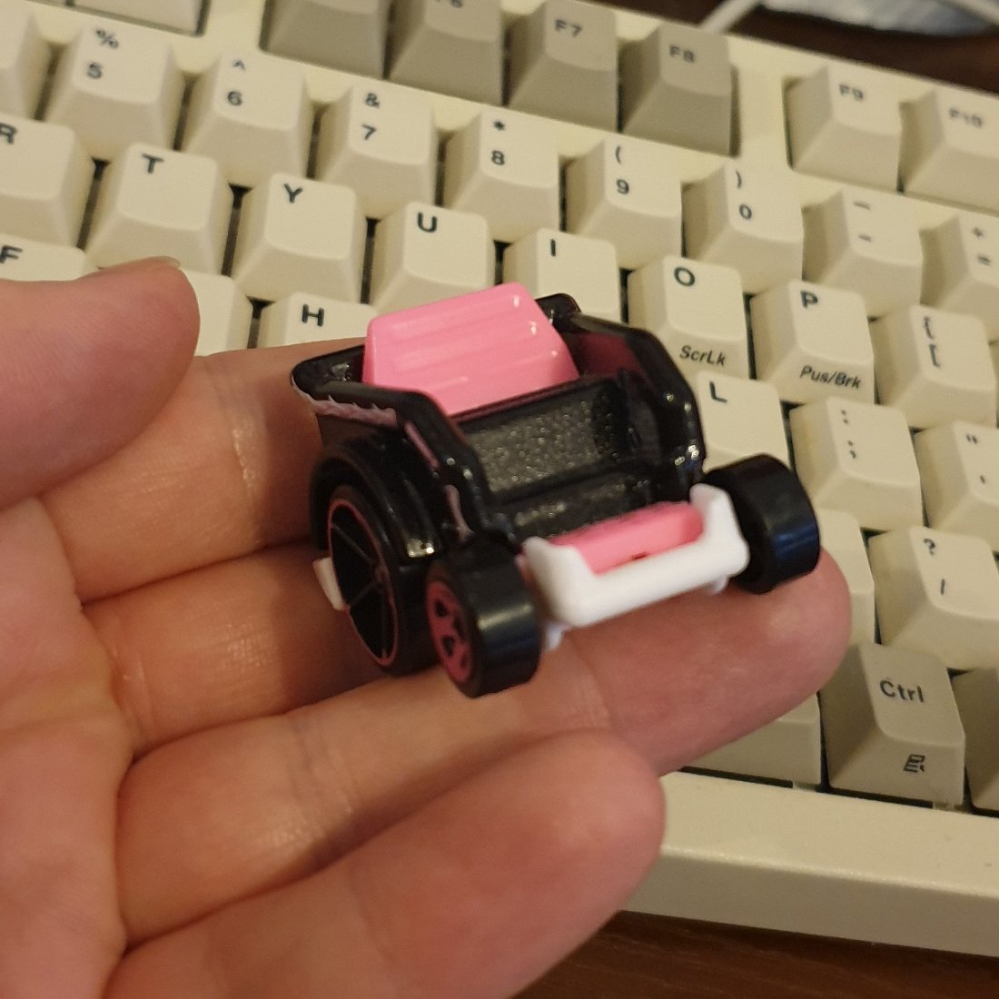 photo of the front of the same small diecast wheelchair. the back rest is hot pink, the seat is black, and the foot rest is white and hot pink.