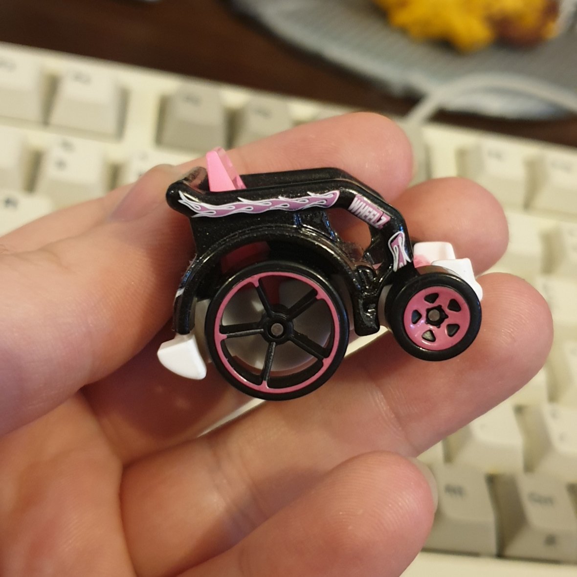 photo of the side of a small diecast wheelchair. the main body is black with a pink flame design and the word 'wheelz'. the rims of the wheels are hot pink.