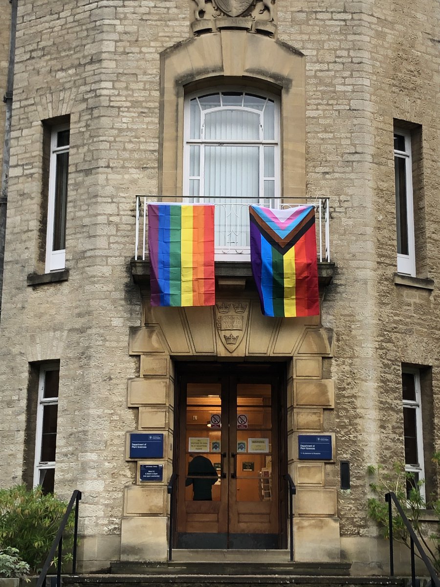 The front of the Plants Sciences building with the rainbow and progress flags displayed above the door