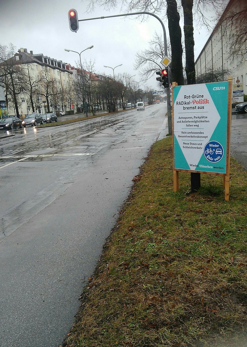 Eine leere Straße mit drei Spuren für den Autoverkehr. Rechts befindet sich ein schmaler Radweg. Neben dem Radweg steht ein Plakat der CSU mit der Botschaft. "Rot-Grüne RADikal-Politik bremst aus"