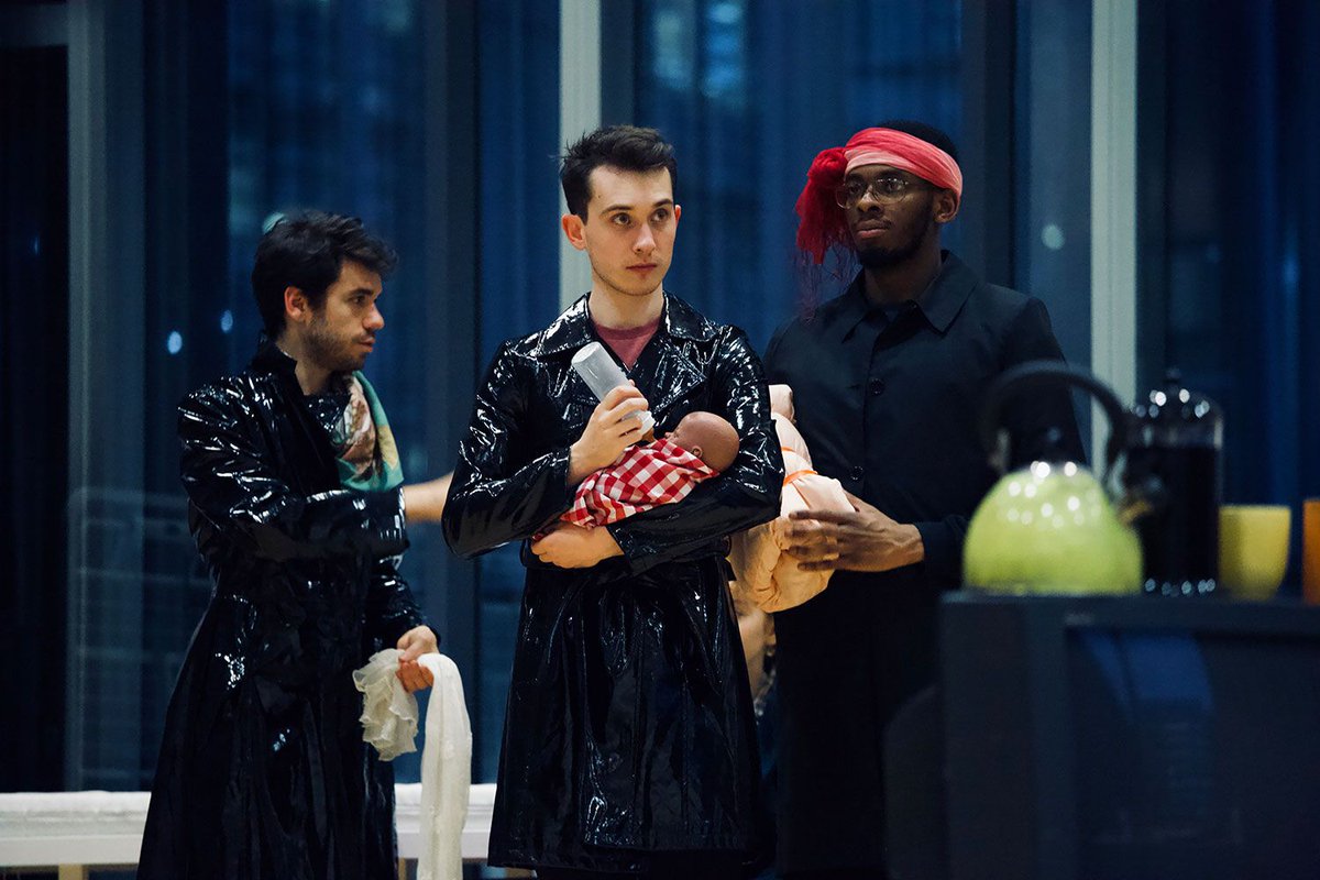 Actors wearing PVC trenchcoats holding dolls