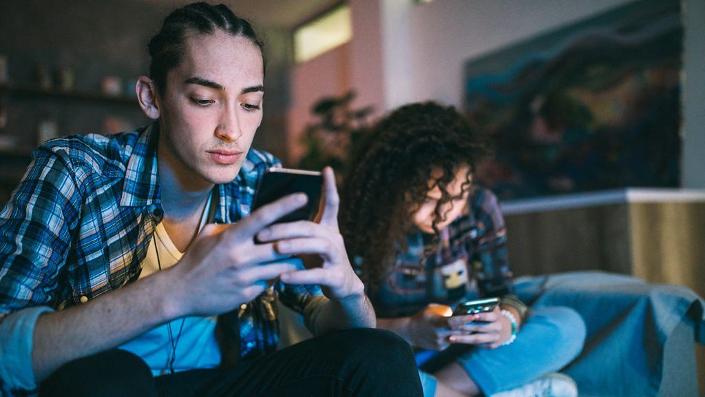 two people sitting side by side, both looking at their phones 